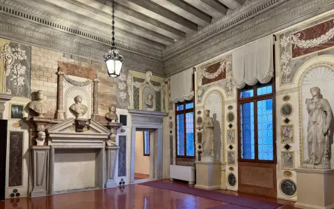 Interni del Palazzo Grimani: busti, statue, camino e finestre decorate in un salone sontuoso.
