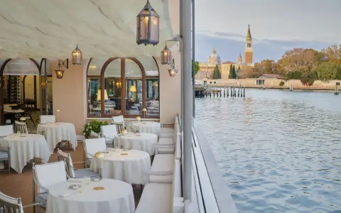 Terrazza elegante di uno dei ristoranti famosi a Venezia, con tavoli apparecchiati e vista sul canale e sulla città.
