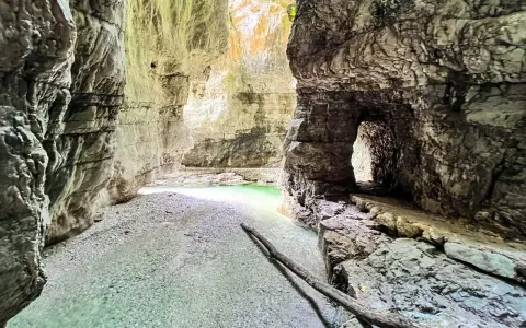 Gola rocciosa con acqua cristallina che ricorda il lago del Mis. Un sentiero scavato nella roccia conduce verso un'apertura luminosa.