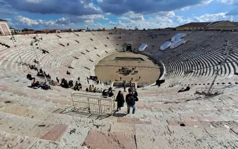 L'**arena di Verona colosseo** romano, con le sue gradinate affollate di turisti, sotto un cielo azzurro e nuvoloso.