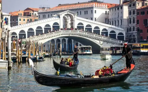 La gondola veneziana scivola sull'acqua, con il Ponte di Rialto sullo sfondo, un'icona di Venezia.