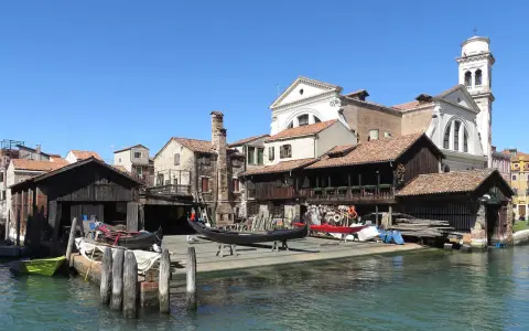 Lo squero di San Trovaso, con gondole in lavorazione e un campanile sullo sfondo, riflette la tradizione veneziana.