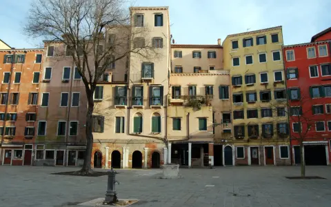 Edifici colorati nel ghetto ebraico di Venezia, con un albero spoglio e una fontana nella piazza lastricata.