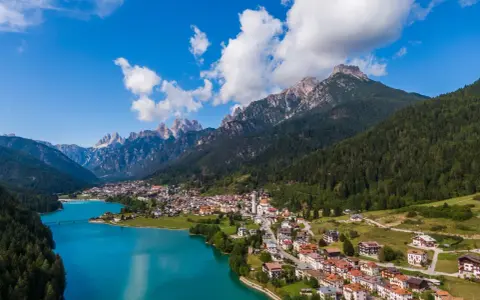 Vista aerea del **lago Auronzo di Cadore** con le montagne sullo sfondo e il paese che si affaccia sull'acqua turchese.