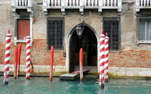 I pali di Venezia, chiamati bricole, segnano il canale davanti a un palazzo storico.