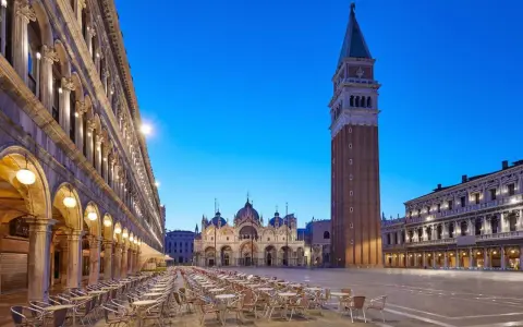 Piazza San Marco a Venezia, con la Basilica e il Campanile, testimoni della ricca storia della città. Tavolini all'aperto creano un'atmosfera serale.
