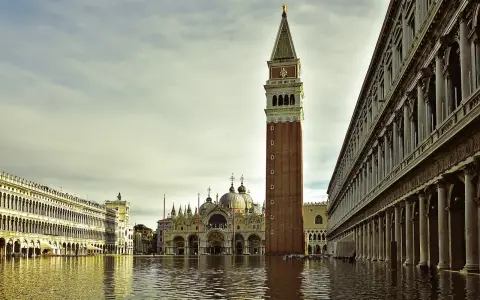 La maestosa torre di Piazza San Marco si erge sull'acqua alta, riflettendosi nel canale che lambisce i palazzi storici.