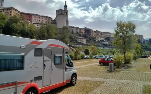 Camper in sosta a Belluno, con case colorate e un campanile sullo sfondo.
