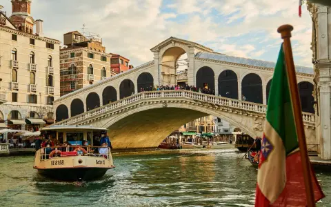 Traghetto della linea 2 di Venezia naviga sul Canal Grande sotto il Ponte di Rialto, con gondole e edifici storici sullo sfondo.