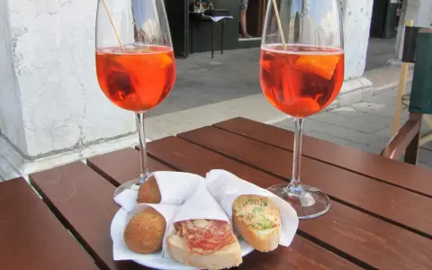 Due calici di Spritz e cicchetti, un classico per gli aperitivi a Venezia, su un tavolino di legno.