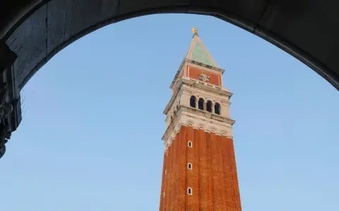 Vista dal campanile di San Marco: la torre in mattoni rossi si staglia contro il cielo azzurro, incorniciata da un arco di pietra.