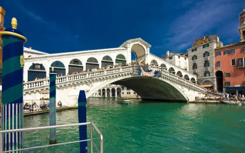Ponte di Rialto, un'icona della storia veneziana, con le sue botteghe e la folla che lo attraversa, si specchia nelle acque verdi del Canal Grande.