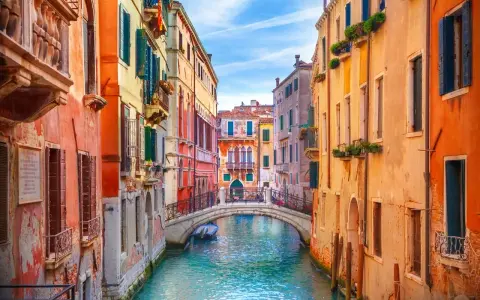 Canale veneziano con palazzi colorati e un ponte. Si immagina come fu costruita Venezia, su palafitte e ingegno.