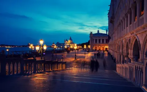 Venezia di notte, con le luci dei lampioni che illuminano la piazza e le sagome sfocate dei passanti.