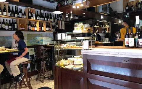 Interno di un'osteria al cicheto a Venezia, con bottiglie di vino, cibi in vetrina e persone sedute al bancone.