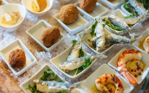 Assaggio di prodotti tipici veneziani: crocchette dorate, sarde fritte e gamberi grigliati, presentati su un letto di ghiaccio.