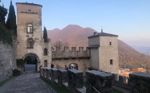 Antico borgo di Cison di Valmarino con torri e mura di pietra, sullo sfondo colline autunnali.