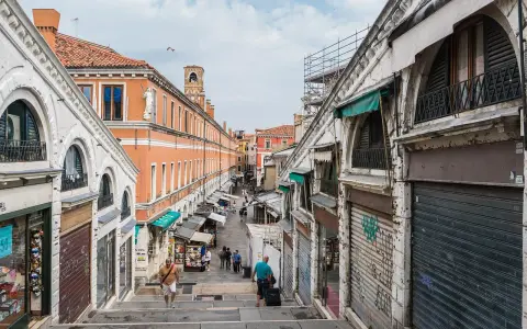 Scendendo le scale del ponte di Rialto a Venezia, si intravede un mercato vivace con negozi e bancarelle.