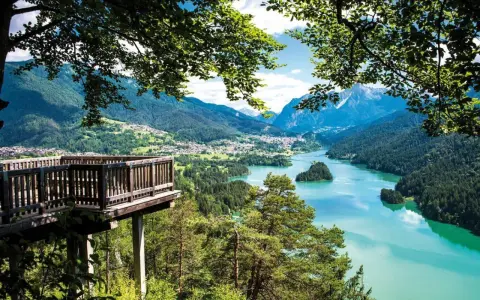 Terrazza panoramica sui laghi del Cadore, con montagne sullo sfondo e un'isola verde nel lago turchese.