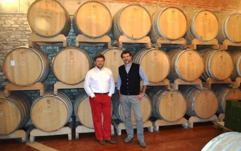 Due uomini in una cantina con botti di legno, simbolo delle migliori cantine dei Colli Euganei.