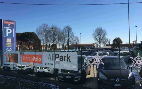 Parcheggio Marco Polo, con bus navetta gratuito per l'aeroporto. Auto parcheggiate dietro una recinzione con decorazioni a fiocco di neve.