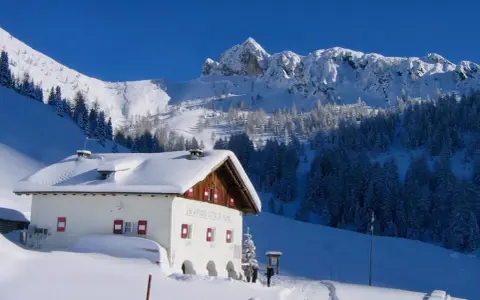 Rifugio innevato nelle Dolomiti, ideale per ciaspolate invernali. Montagne maestose e boschi coperti di neve.