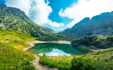 Sentiero panoramico verso un lago alpino turchese, incorniciato da montagne maestose. Un vero gioiello dell'alta via Dolomiti più bella.
