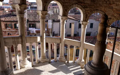 Dalla scala Contarini del Bovolo, vista sui tetti di Venezia. Colonne e archi in pietra creano un gioco d'ombre sulla gradinata.