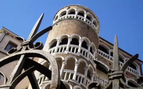 La Torre del Bovolo, con la sua architettura a chiocciola e i suoi loggiati, si staglia contro il cielo azzurro, vista attraverso un cancello in ferro battuto.