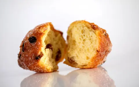 Frittelle veneziane, dolci e soffici, con uvetta e zucchero, spezzate a metà per mostrare l'interno invitante.