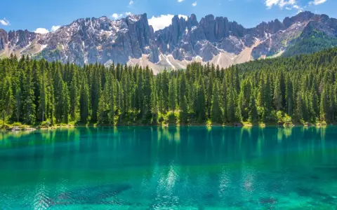 Lago alpino dalle acque turchesi, circondato da una fitta foresta di abeti, con le maestose cime delle Dolomiti innevate sullo sfondo. Un paesaggio da sogno, tra Venezia e le Dolomiti.