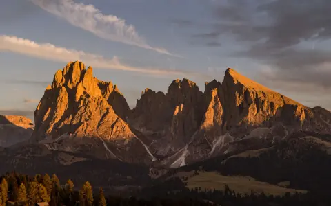 Le maestose **Dolomiti Rosse** illuminate dal sole al tramonto, con cime aguzze e pendii boscosi.