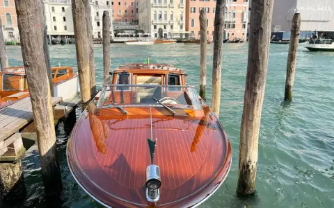 Un elegante taxi boat in legno lucido attende sul Canal Grande a Venezia, pronto a trasportare passeggeri tra i palazzi storici.