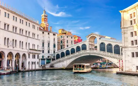 Venezia, il Canal Grande con il Ponte di Rialto e il Fondaco dei Tedeschi sullo sfondo. Una motonave naviga sull'acqua.