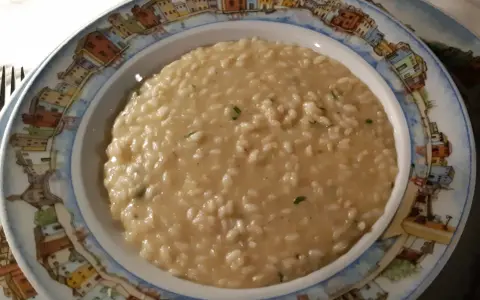 Un cremoso risotto di go Burano, servito in un piatto decorato con le case colorate dell'isola.