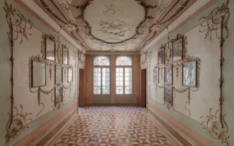Corridoio decorato con stucchi dorati e specchi, soffitto affrescato e pavimento a rombi. Un assaggio dell'eleganza del Casino Venier.