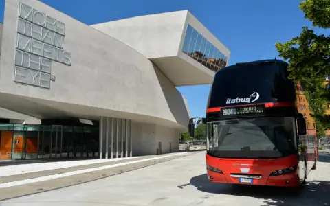 Autobus Itabus rosso e nero davanti a un edificio moderno con la scritta "More Than Meets The Eye". Un viaggio da Verona a Jesolo?