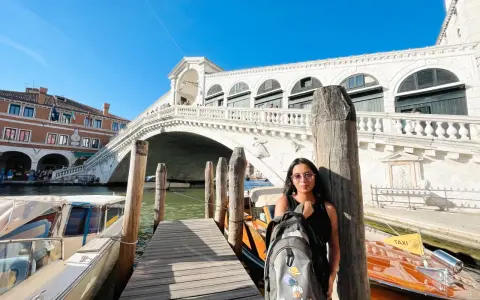 Una splendida giornata a Venezia, con la giovane donna che posa con il suo zaino davanti al Ponte di Rialto e ai taxi d'acqua.