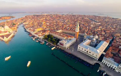 Vista aerea di Venezia al tramonto, con la Basilica di San Marco e il Palazzo Ducale che dominano la scena.