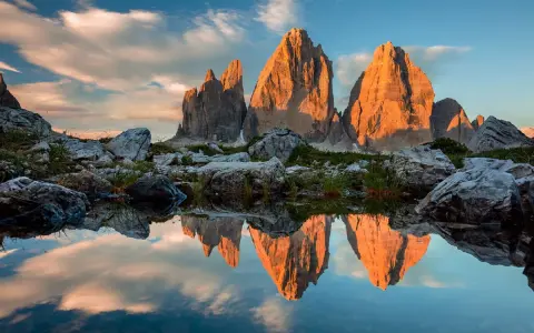 Le Tre Cime di Lavaredo illuminate dal tramonto, riflesse in uno specchio d'acqua. Un paesaggio che incarna la bellezza dei **Dolomiti paesi più belli**.
