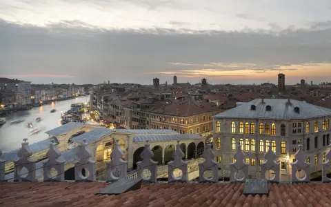 Vista dal **fondaco dei tedeschi Venezia terrazza** al tramonto, con il Canal Grande e il Ponte di Rialto illuminati.