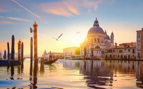 Gondola che scivola sull'acqua al tramonto, con la Basilica di Santa Maria della Salute sullo sfondo. Un'indimenticabile attività a Venezia.