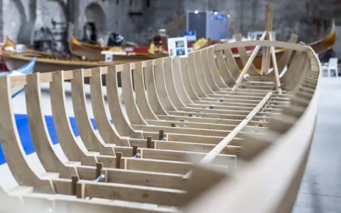 Struttura in legno di una barca veneziana in costruzione, con altre imbarcazioni sullo sfondo.