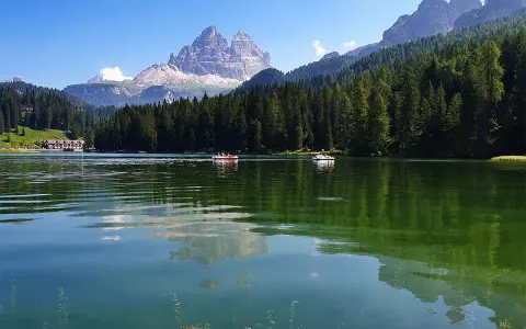 Il **lago di Misurina** incanta con le sue acque verdi e le montagne maestose. Barchette a remi solcano la superficie, riflettendo il cielo azzurro e la foresta di abeti.