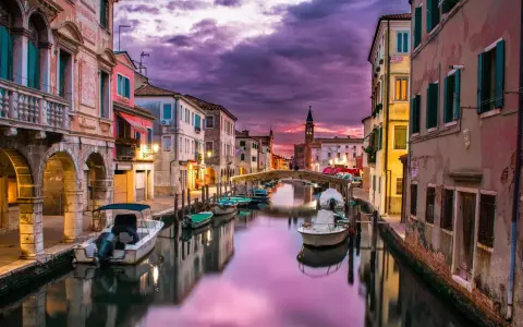 Un canale di Venezia al tramonto, con barche ormeggiate e riflessi viola sull'acqua. Un'atmosfera magica che ricorda i piombi di Venezia.