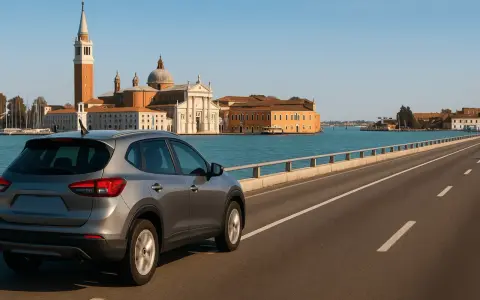 Un'auto grigia percorre il ponte verso Venezia, con la Basilica di San Giorgio Maggiore e il campanile che si stagliano sullo sfondo.