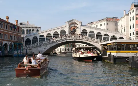 Gondola e vaporetti navigano sul Canal Grande sotto il maestoso Ponte di Rialto, un'icona di Venezia.