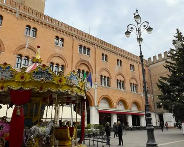 Carosello colorato e albero di Natale in piazza, scorci di cosa vedere a Treviso con palazzi storici e gente che passeggia.