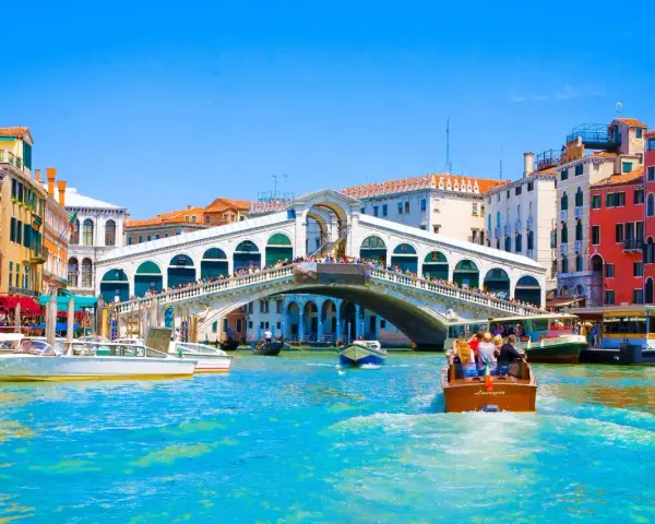 Gondole e vaporetti solcano il Canal Grande, sotto il Ponte di Rialto affollato di gente. Un assaggio delle **esperienze Venezia**.