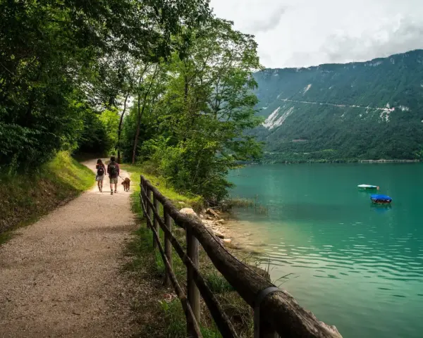 Coppia con cane passeggia lungo il sentiero del lago di Santa Croce, godendosi la natura e il panorama montano.